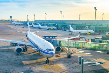 Glass jet bridge passage, airplanes by terminal in sunset light, buses, airfield, of Barcelona International Airport, Spain