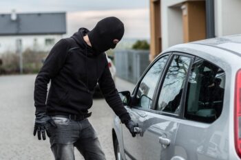 Man dressed in black with a balaclava on his head pulls the handle of a car. Car thief, car theft concept