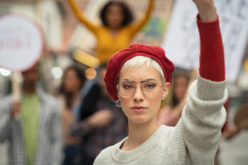 Woman leading a group of demonstrators on road for women rights. Young strong woman protest during a global strike. Portrait of angry girl in rally to protest on climate change looking at camera.